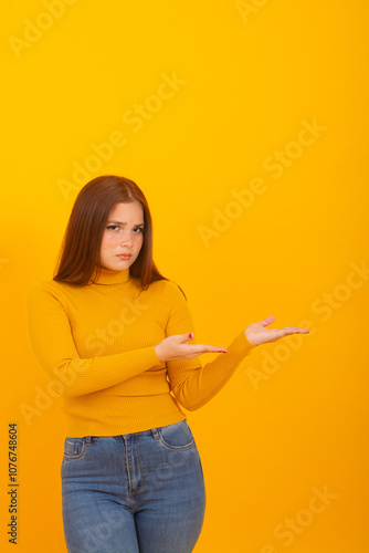 Serious Young Redhead girl pointing Both Hands to right isolated on yellow background