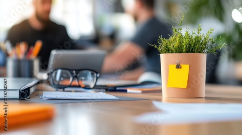 A modern office desk with a small potted plant and a blurred background featuring two workers discussing, symbolizing productivity and teamwork. photo