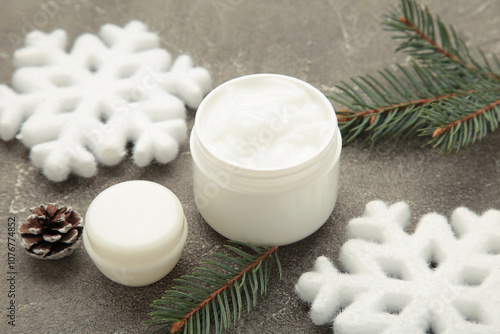 Cold protecting winter cream concept. Jar cosmetics with snowflakes and fir tree branches on grey background. Winter seasonal skin care photo