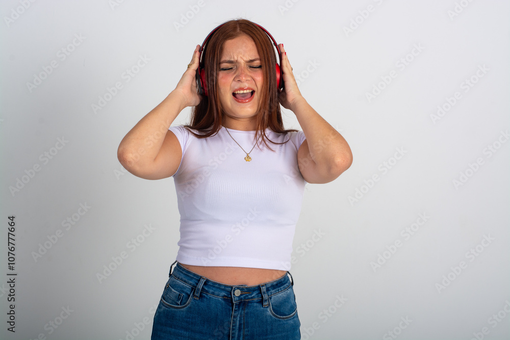 Horizontal portrait with copy space of a beautiful red head lady singing ant listening to music with eyes closed touching her head isolated on white background Horizontal portrait with copy space of a beautiful red head lady singing ant listening to music with eyes closed touching her head isolated on white background
