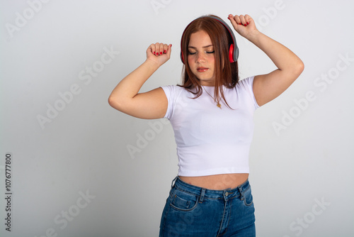 Medium long shot of a dancing latin redhead young lady listening to music and wearing red headphones on a isolated white background photo