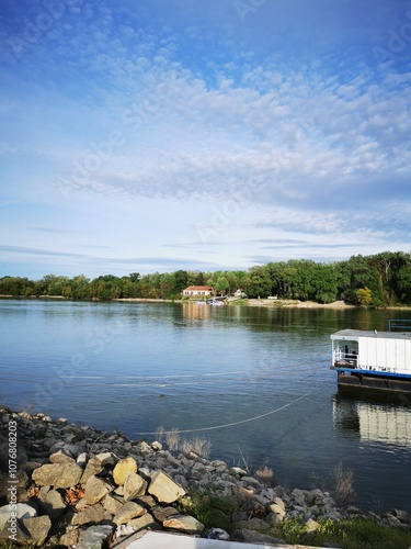 Tranquil river view with a boat anchored by rocky shore on a sunny day near lush green trees photo