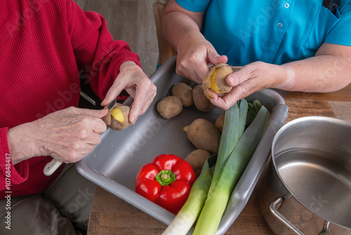 Preparing dinner in a care home. Elderly woman peeling potatoes.