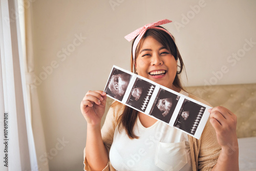 Smiling pregnant woman holding ultrasound photos, expressing joy and excitement about her pregnancy, wearing a pink headband and casual clothing photo