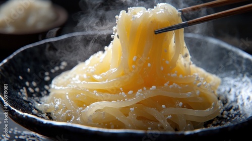 Steaming bowl of udon noodles with sesame seeds.