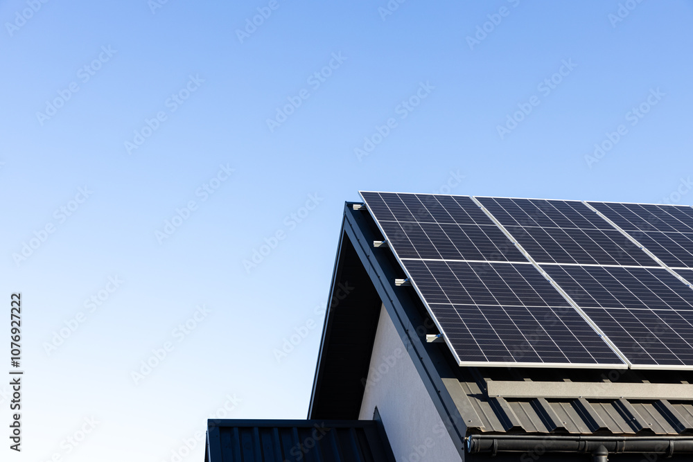 Fototapeta premium Modern house with solar panels stand-alone photovoltaic plant system on household metal sheet rooftop. Clear blue sky background. Clean alternative energy concept. Professional installation, go green
