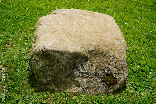 A large weathered rock sits in a field of lush green grass. This natural stone could be used for landscaping or as a garden feature.