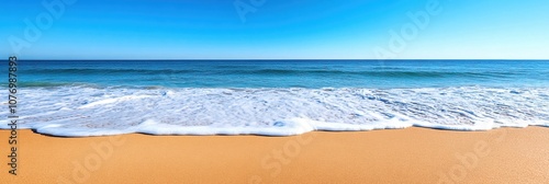 Calm ocean waves lapping at the sandy shore under a clear blue sky.