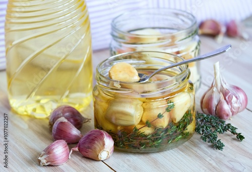 Spoon with garlic clove pickled in sunflower oil and thyme.  A glass jar full of garlic cloves should be kept in the refrigerator.