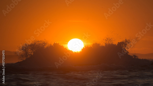 Silhouette of a breaking sea wave against the setting sun