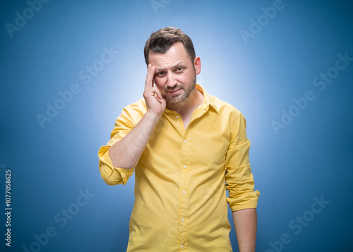 Tired man looking at camera over blue background, dresses in yellow shirt. Exhausted guy with sleepy expression photo