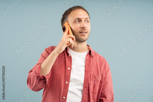 Interesting conversation. Focused man holds smartphone to ear to answer call. Smiling thoughtful guy talking on phone at leisure, discussing pleasant news, getting favorable offer isolated studio wall photo