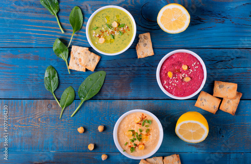 Colorful hummus in white bowls on blue wooden table. Classic, beetroot and spinach chickpea dips. Vegetarian dish. Middle Eastern cuisine