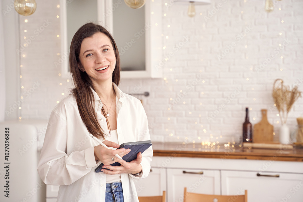 Smiling woman using tablet in cozy kitchen with warm lighting and string lights. Smiling woman using tablet in cozy kitchen with warm lighting and string lights.