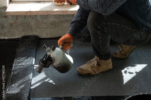 Waterproofing the floor in the house, a man heats a bitumen roll with a kerosene lamp. photo