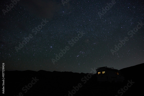 Starry night sky over mountains with illuminated cabin in the foreground