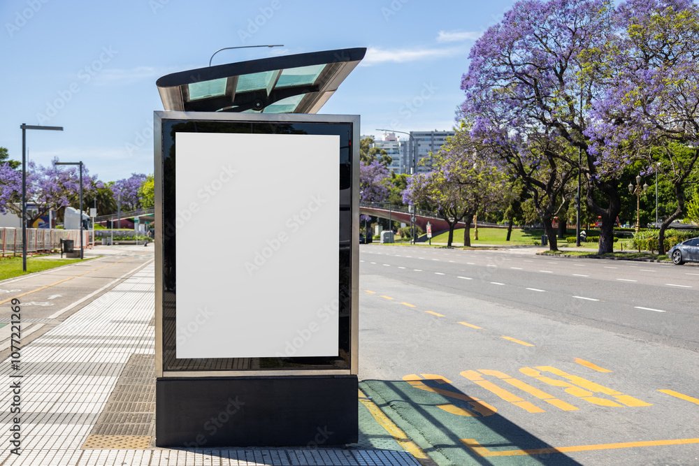 Vertical blank billboard at a bus stop shelter in Buenos Aires, Argentina with jacaranda trees blooming along Libertador avenue in spring. Copy space poster on a lightbox for displaying ad content