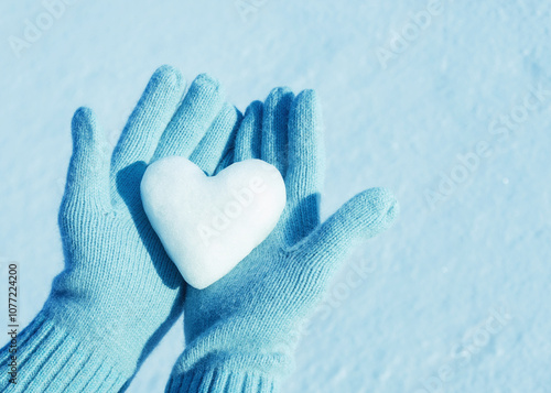  A woman's hands in knitted gloves  with heart of snow. Love concept. Valentine day concept.	