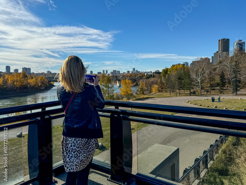 Edmonton, Alberta - October 13, 2024: A woman taking pictures of the views of the Edmonton skyline with the North Saskatchewan River in the foreground
