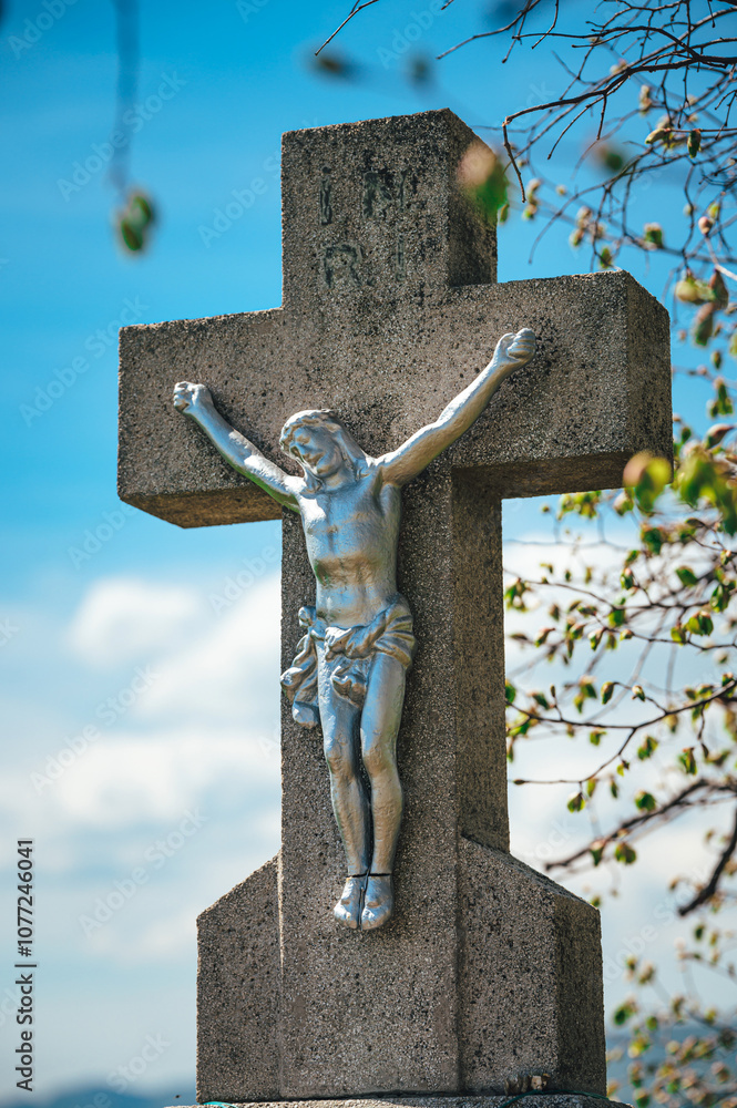 Fototapeta premium Christian Stone Cross with Statue of Jesus Christ, a Sacred Place for Prayer, Reflection, Rest, and a Symbolic Memorial for Departed Loved Ones