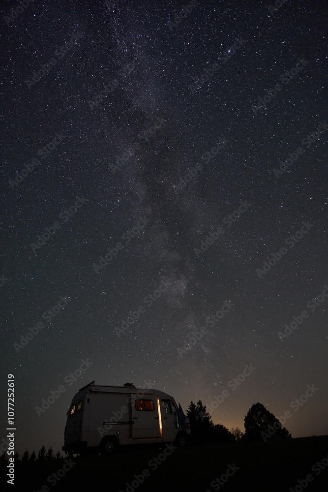 Fototapeta premium Starry night sky over camper van parked in a remote area with the Milky Way visible