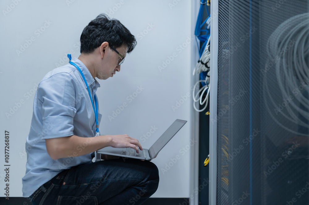 Fototapeta premium Computer engineer is setting up network in server room,Systems Maintenance Technician,Male engineer working in server room at modern data center