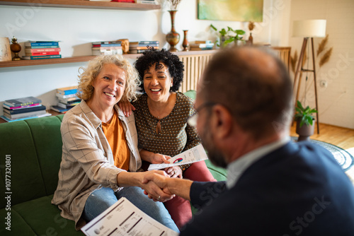 Lesbian couple talking to financial advisor at home shaking hands photo