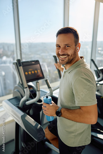 Happy athletic man practicing on elliptical trainer at health club and looking at camera. photo