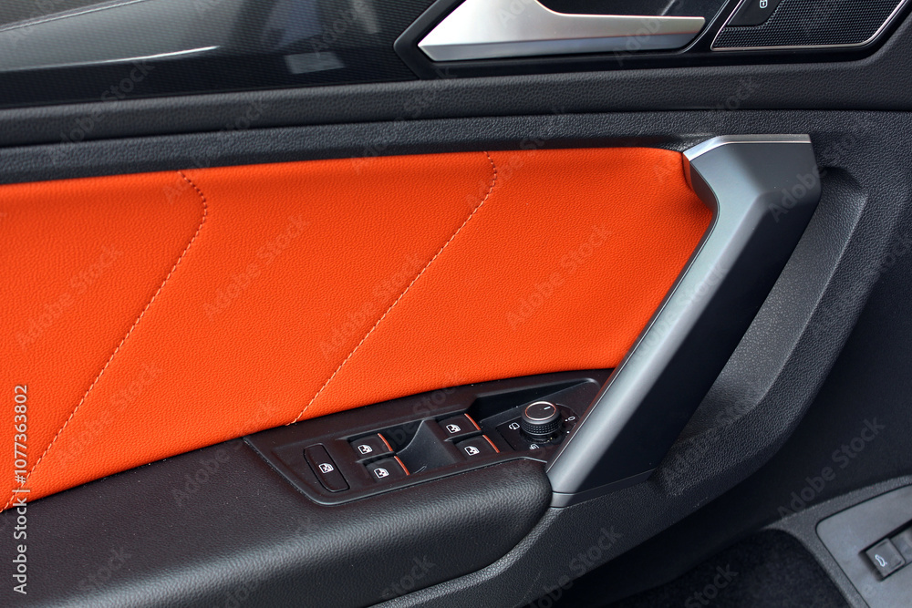 Fototapeta premium Orange interior of sports crossover. Car leather Orange interior details of door handle with windows controls and adjustments. Modern car orange leather interior. Sports car interior.