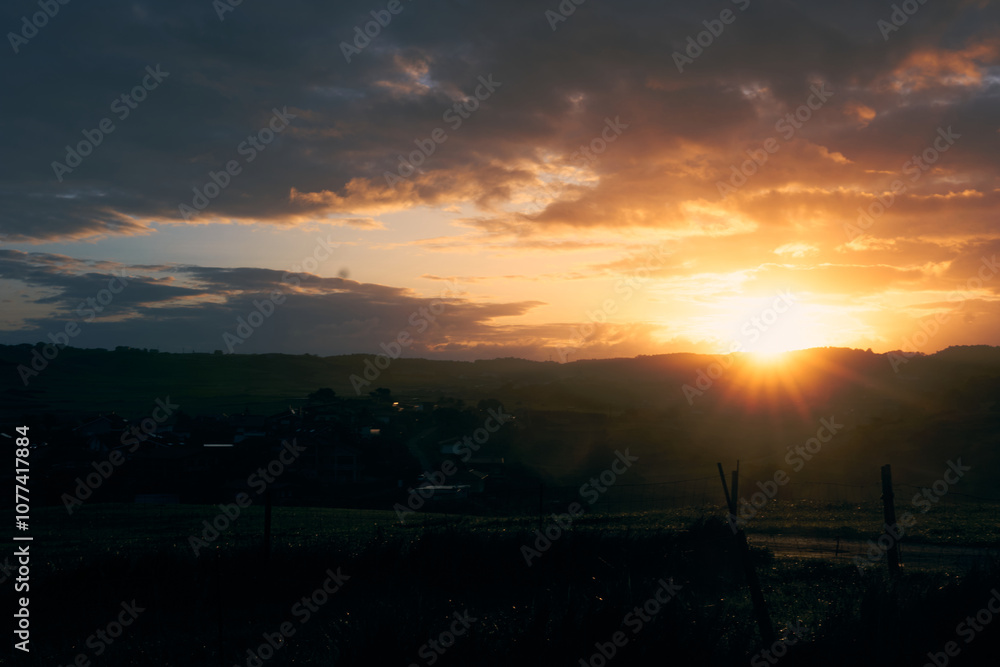 Naklejka premium Sunrise over rolling hills creating a golden glow in a quiet countryside landscape