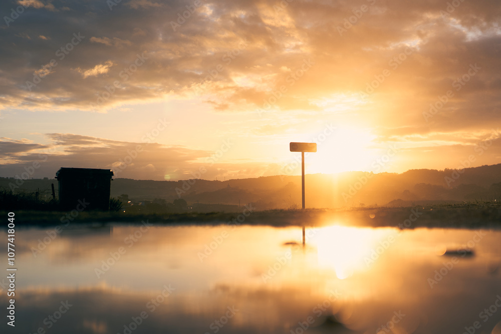 Sunset over the hills with reflective puddle and distant sign in a serene landscape Sunset over the hills with reflective puddle and distant sign in a serene landscape