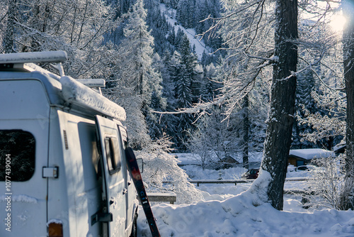 Snowy landscape with a camper van surrounded by frosted trees and mountains in winter