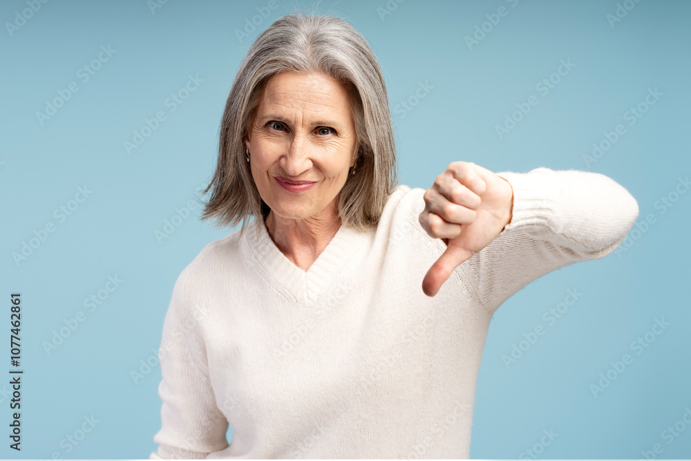 Fototapeta premium Portrait of serious senior woman showing dislike, looking at camera thumb down