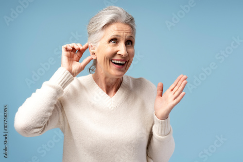 Happy, attractive senior woman having hearing aid in ear, posing isolated on blue background photo