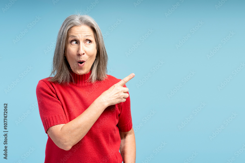 Portrait of excited, happy mature woman wearing red sweater pointing finger on copy space Portrait of excited, happy mature woman wearing red sweater pointing finger on copy space