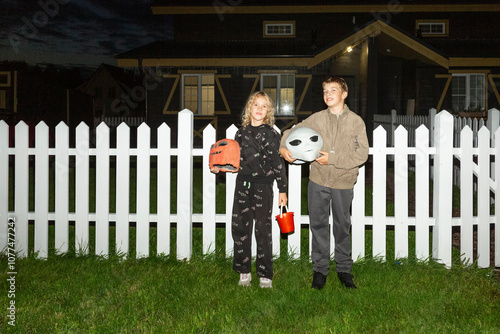 Children holding Halloween masks by a white picket fence

 photo