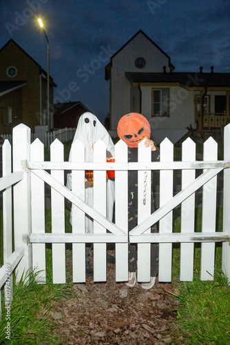 Children in Halloween costumes standing behind a white picket fence

 photo