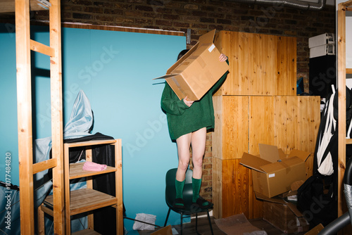 Person Balancing on Chair Holding Cardboard Box in Storage Room photo