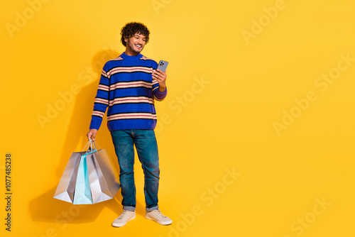 Full size photo of pretty young male hold gadget shopping bags wear trendy blue striped outfit isolated on yellow color background