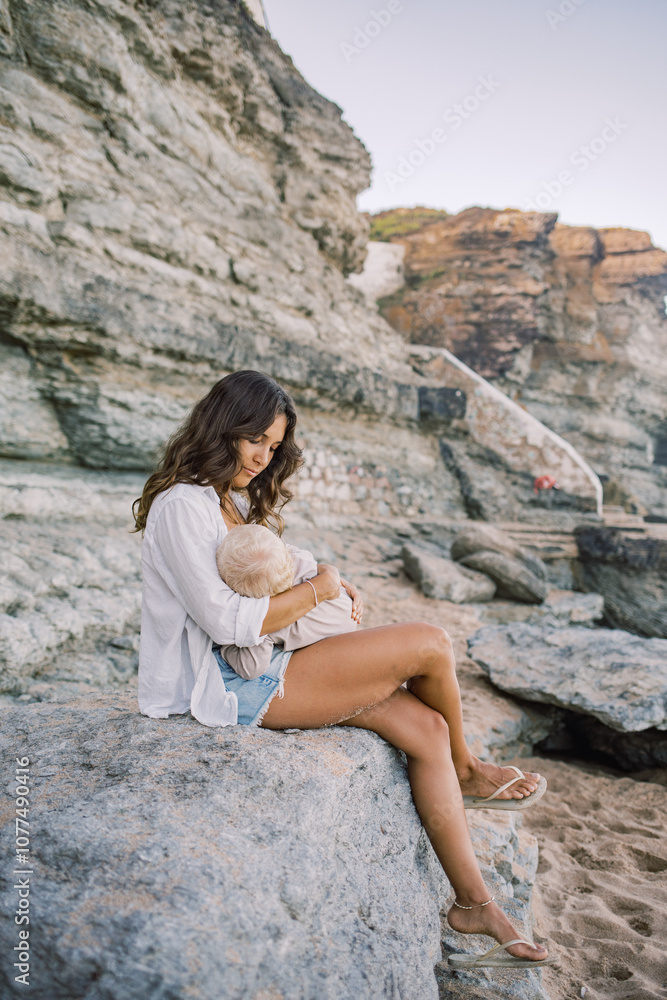 Mother holding smiling baby while sitting on a rock at the beach Mother holding smiling baby while sitting on a rock at the beach