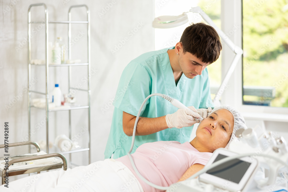 Fototapeta premium Using device and hydrogen oxygen cleaning attachment, young specialist meticulously performs procedure, improving texture and appearance of young woman's skin.