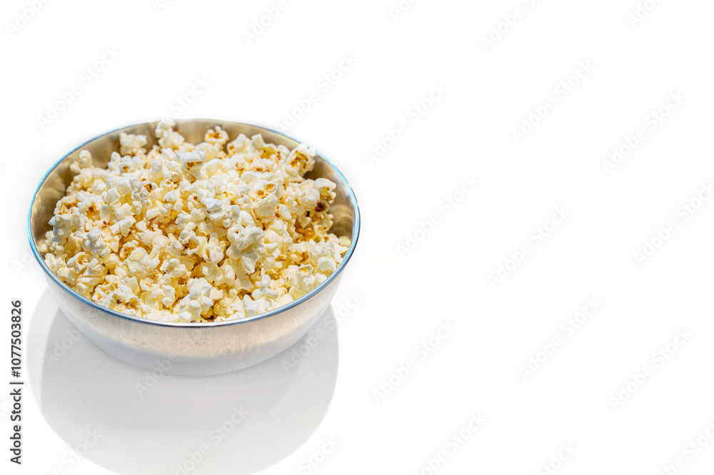 Popped popcorn in an aluminum bowl on a bright white countertop with copy space. Selective focus on the popcorn.