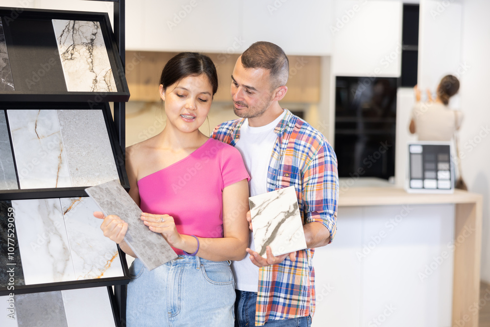 Couple of young man and woman customers selecting tiles from samples in hardware store Couple of young man and woman customers selecting tiles from samples in hardware store