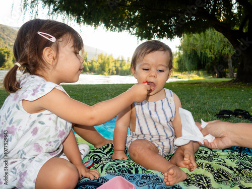 Little girl feeding her baby brother with a spoon on a picnic photo