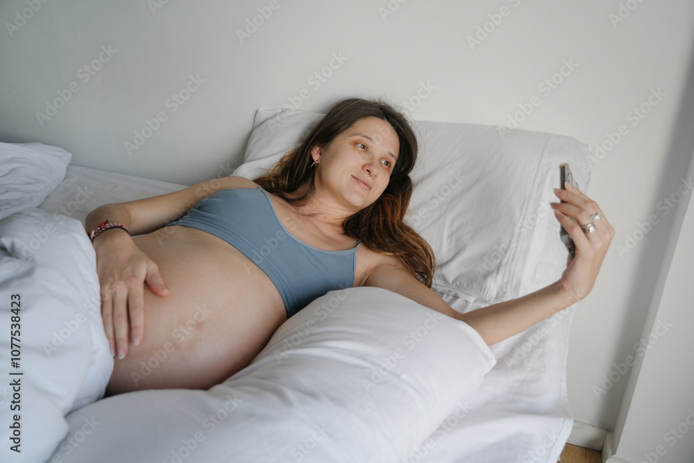Pregnant woman making a video call in bed using her smartphone Pregnant woman making a video call in bed using her smartphone