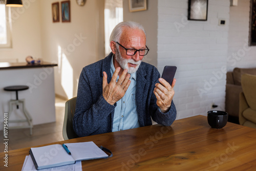 Senior man waving hand at mobile phone photo