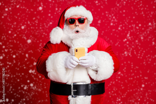 Photo of retired old man grey beard hold telephone shocked impressive news north pole flight available wear santa x-mas costume gloves coat sunglass headwear isolated red color background