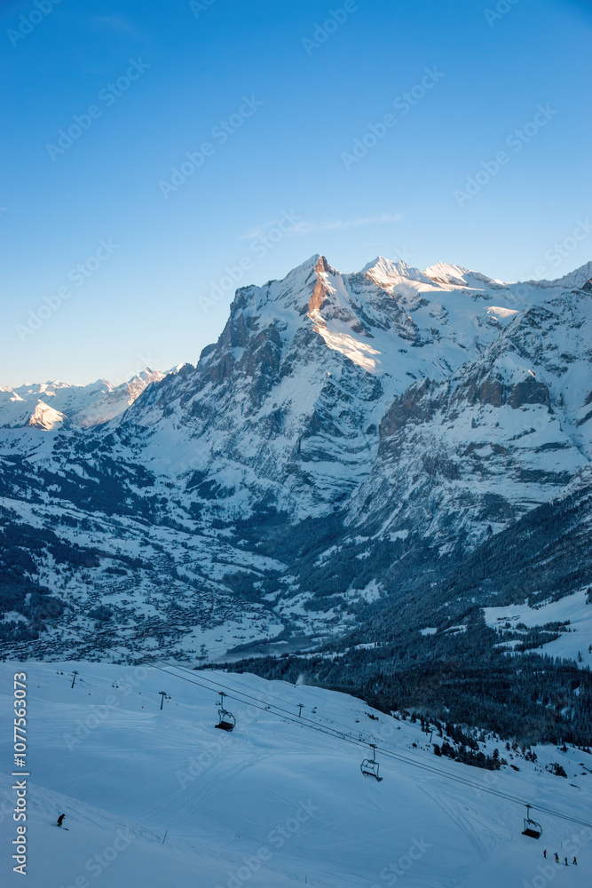 Scenic view of Grindelwald, Switzerland with snowcovered Wetterhorn mountain in winter against blue sky early in the morning