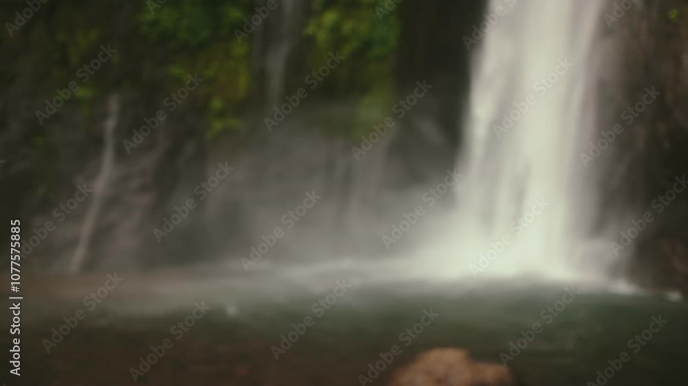 Young female tourist is enjoying the stunning view of a majestic waterfall cascading down a lush cliff in a tropical rainforest