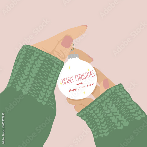 Female hands in a green sweater hold a white ornament with the inscription Merry Christmas and Happy New Year